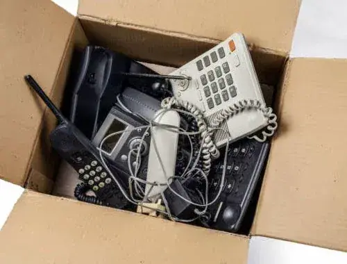 Ausgemusterte Telefone und Elektrogeräte in einem Karton, sortiert zur Entsorgung